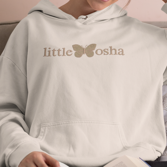 Woman wearing a hoodie with 'little koshka' text, sitting on a couch with an open book.